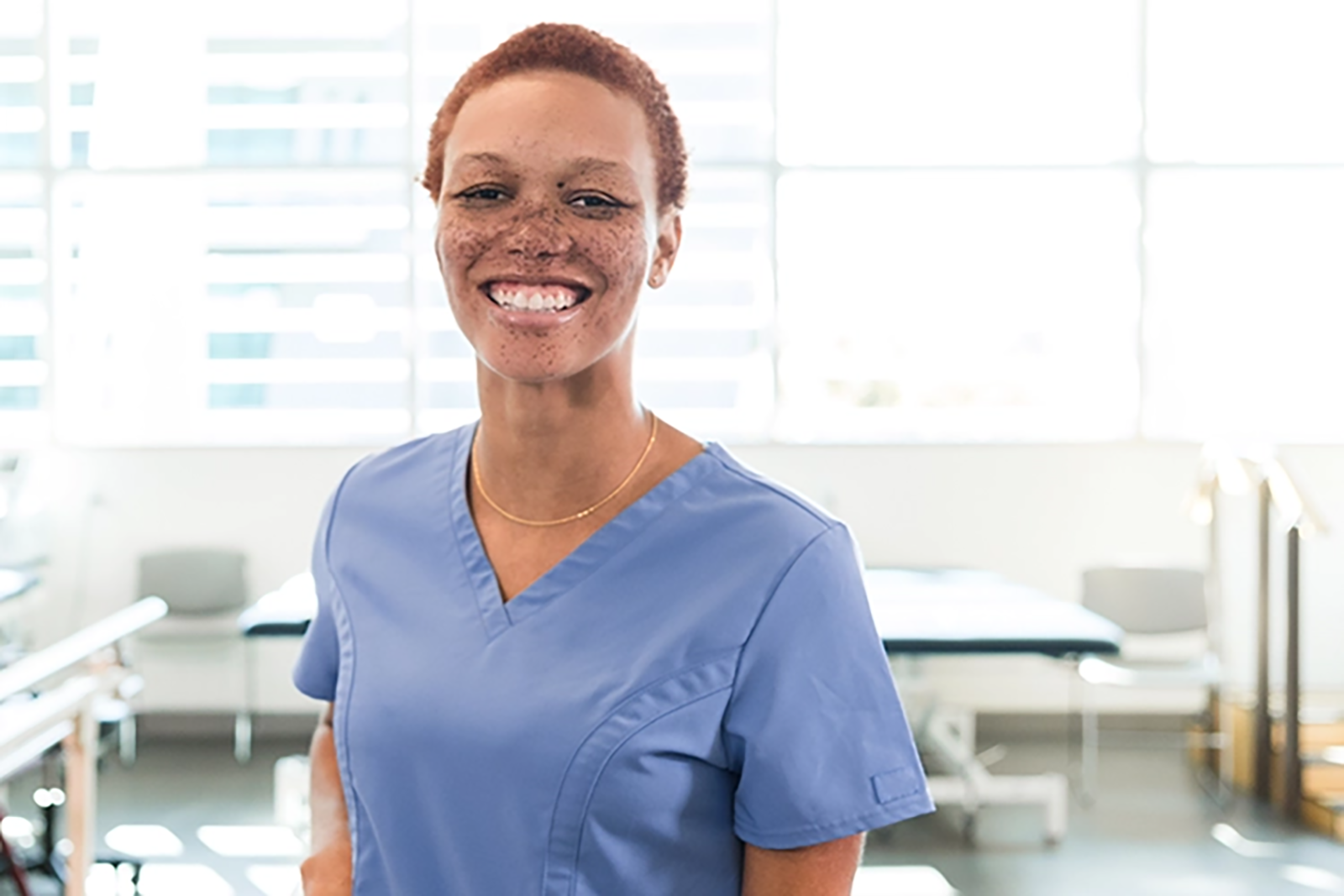 Gaining Confidence_GettyImages-2196795070_WebExclusive A Black woman in scrubs smiles at the camera in a therapy facility.