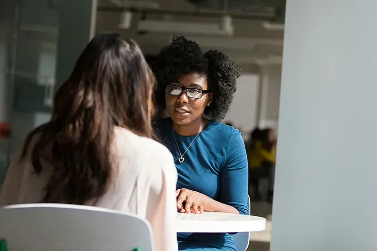 Two women at a table are seated talking.