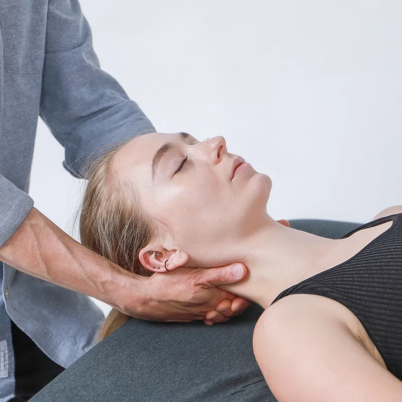 A massage therapist puts both hands under the back of the neck of a supine female client.